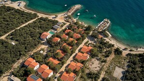 Vista aerea di una zona residenziale costiera con case dai tetti in tegole rosse, una spiaggia e acque blu cristalline.