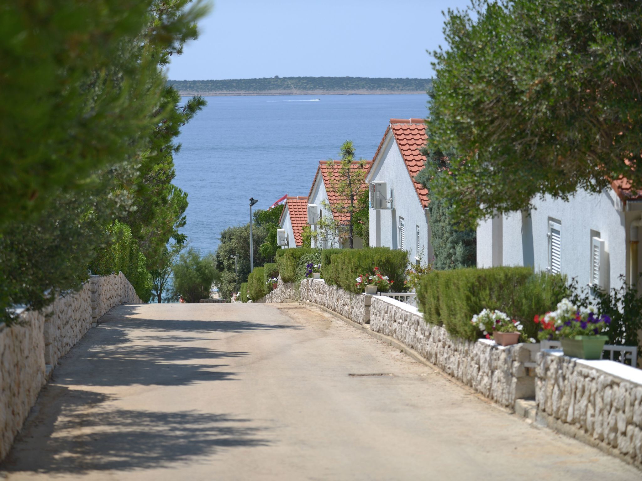 A coastal street with stone walls, white houses with red roofs, and a view of the sea.