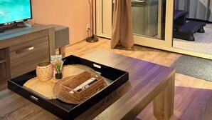 A cozy living area with a wooden bench, a TV on a wooden stand, a tray with a woven basket, and a sliding glass door leading to a balcony. - Wellness-Ferienhaus für 5 Personen by Interhome (Stavenisse)