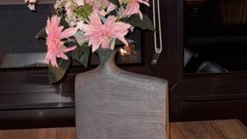 A wooden table with a vase of pink flowers, a small potted plant, candles, and a pink book on a tray.