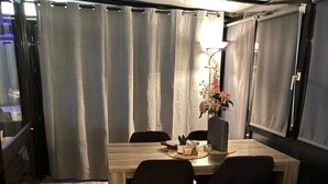A dining area with a wooden table, four chairs, a vase with flowers, and curtains. - Wellness-Ferienhaus für 5 Personen by Interhome (Stavenisse)
