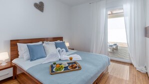 A neatly made bed with a tray of fruits and a drink, a heart-shaped decoration on the wall, and a view of the balcony through sheer curtains. - Wohnung mit schöner Terrasse by Interhome (Crikvenica/Dramalj)