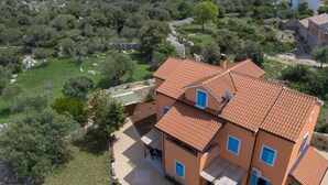 Uma casa de dois andares com telhado de cerâmica, cercada por vegetação e colinas.