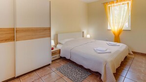 Quarto com cama, luminárias de cabeceira, mesa de cabeceira, guarda-roupa e janela com cortinas.