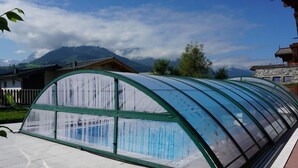 Une serre dotée d’une structure et d’un toit en verre incurvé, installée sur une terrasse carrelée.