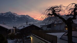 Un village enneigé, avec ses maisons traditionnelles, un escalier en bois et une chaîne de montagnes en arrière-plan.