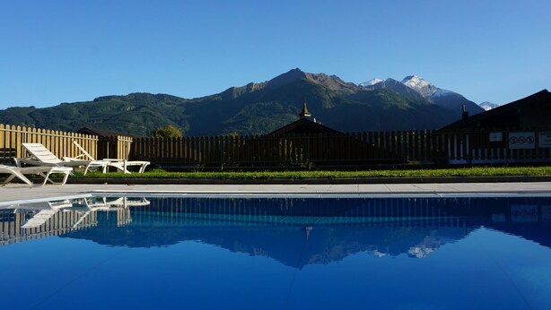 Une piscine avec des chaises longues et une clôture en bois, avec des montagnes en arrière-plan.