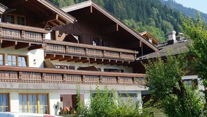 Un immeuble à plusieurs étages, doté de balcons en bois, se dressant sur un fond de montagne boisée.