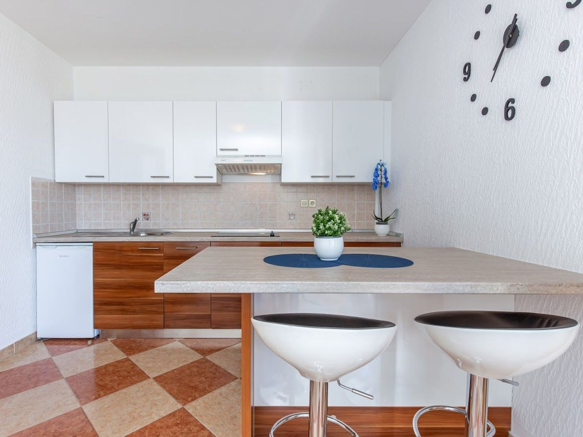 A modern kitchen with white cabinets, a built-in oven, a sink, and a clock on the wall.