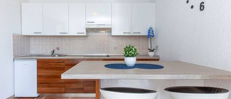A modern kitchen with white cabinets, a built-in oven, a sink, and a clock on the wall.