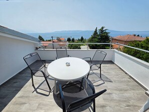 Una mesa redonda con cuatro sillas en un balcón que ofrece vistas al mar y montañas lejanas.
