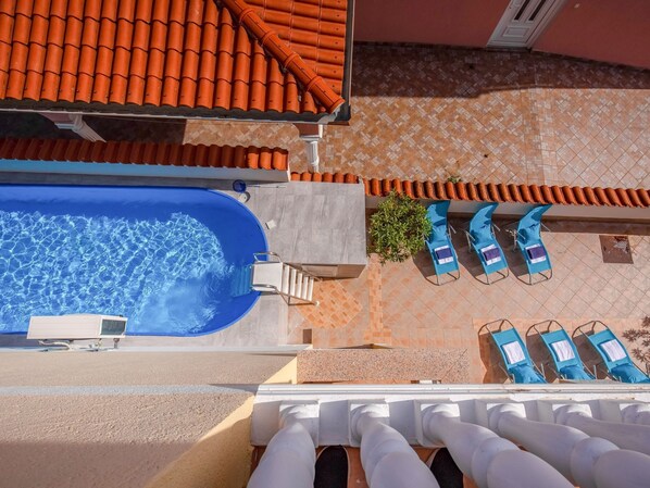 Eine Vogelperspektive auf einen Poolbereich auf einem Dach, mit einem blauen Schwimmbecken, Liegestühlen und einem gefliesten Dach.