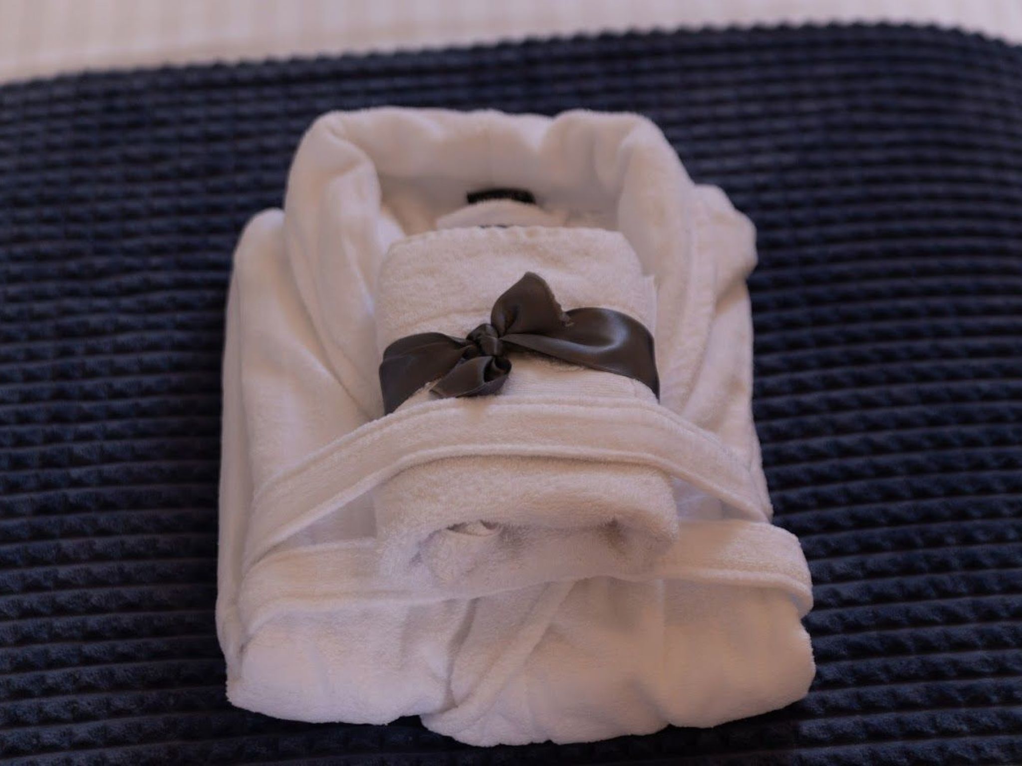 A neatly folded white towel with a dark bow, placed on a textured dark surface.