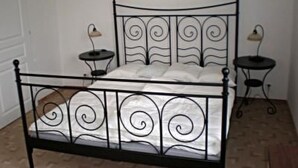 Una cama con estructura metálica, cabecera y piecera decorativos, dos mesitas de noche con lámparas y una decoración con forma de corazón en la pared.