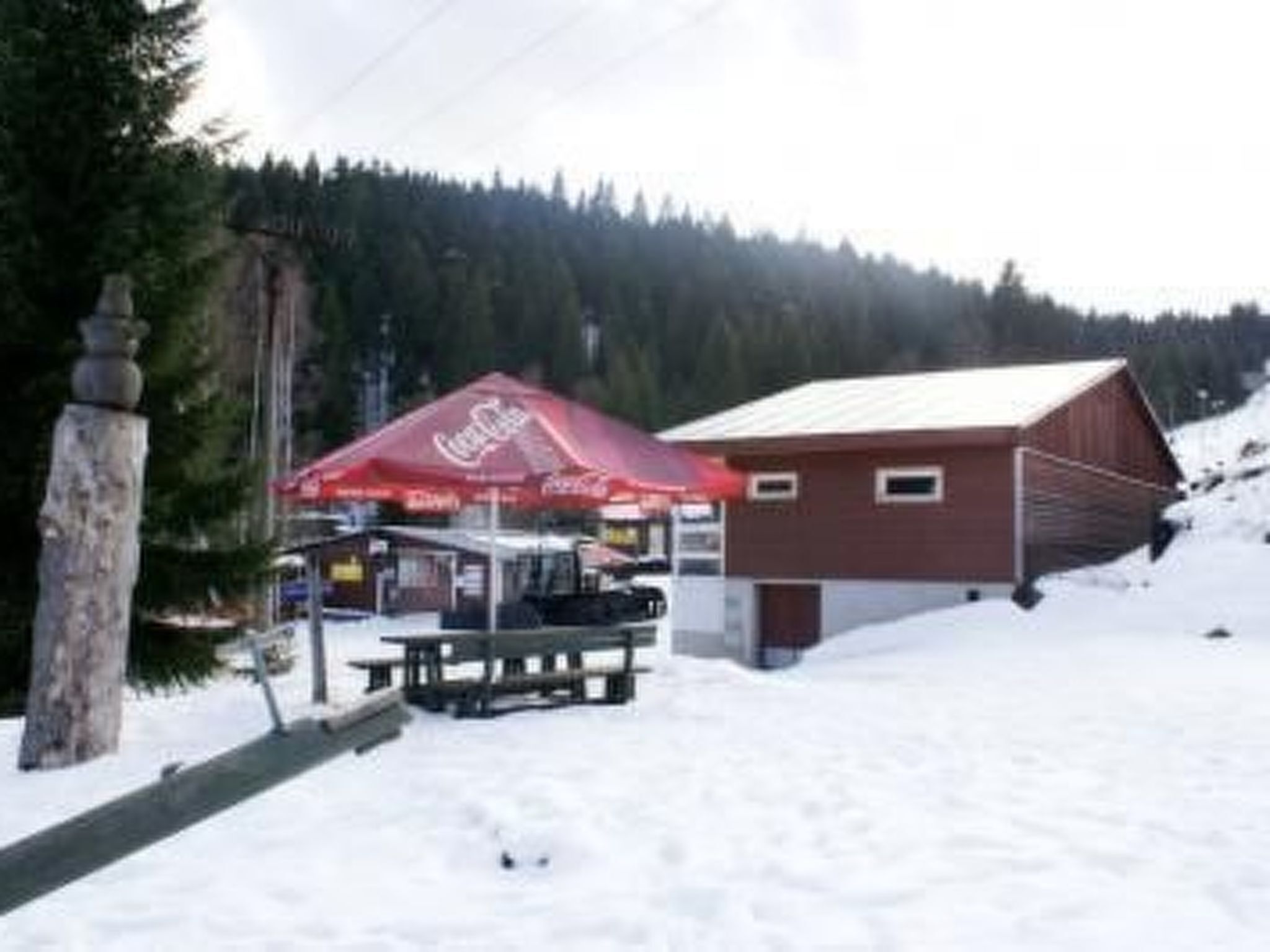 A snow-covered outdoor area with a red Coca-Cola branded tent and a wooden building.