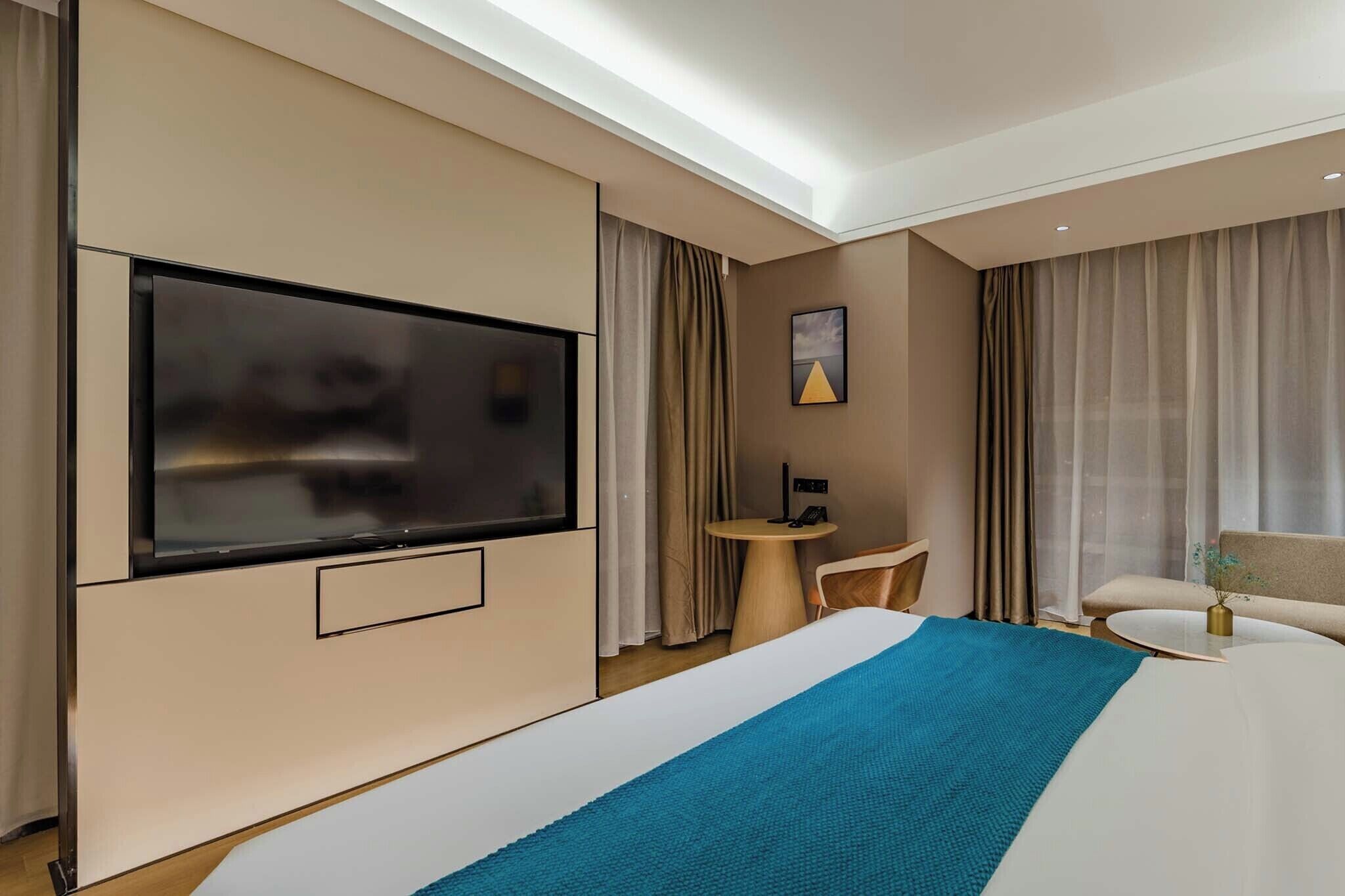A modern hotel room with a large bed, a flat-screen TV, a small round table, and a sofa.