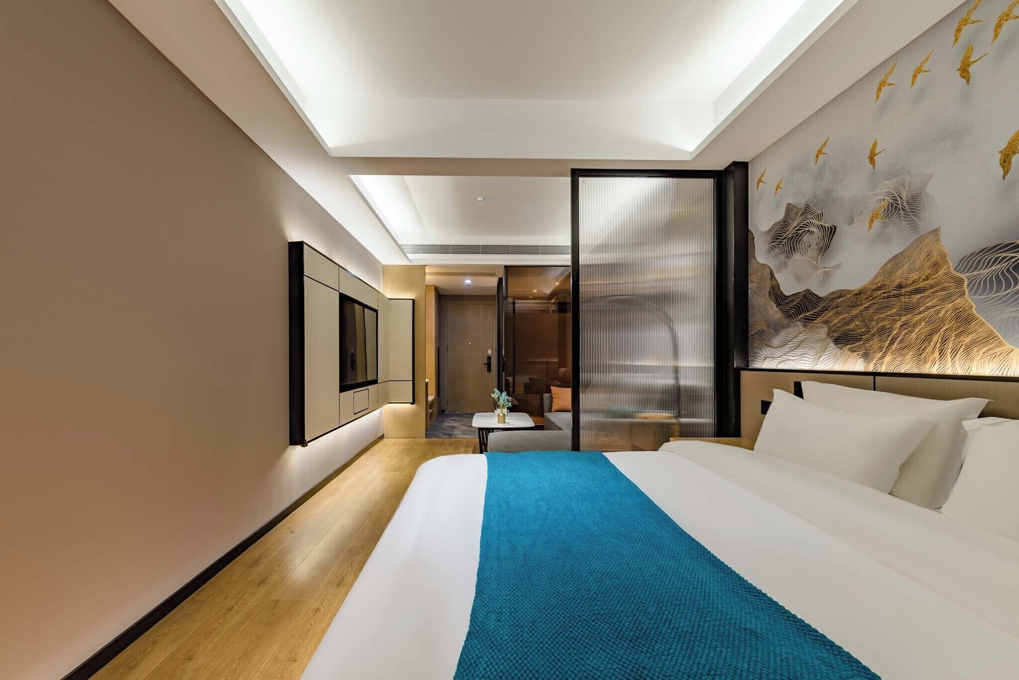 A modern hotel room with a large bed, a bedside table, a wall-mounted TV, and a decorative mural.