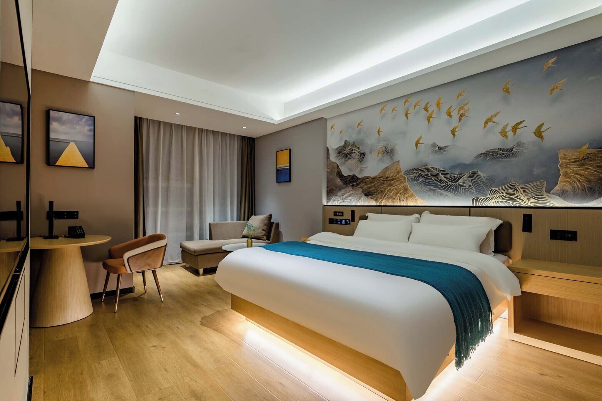 A modern hotel room with a large bed, a desk, a chair, and a large wall mural.
