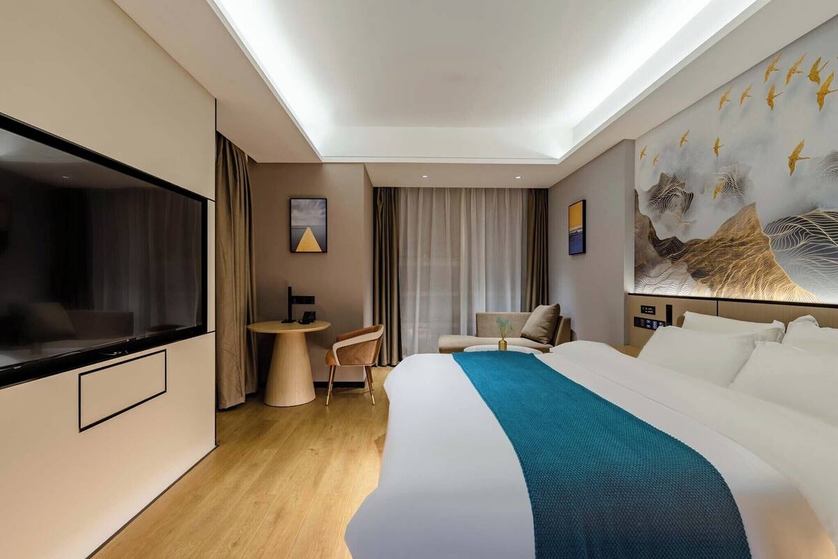 Una habitación de hotel moderna con una cama grande, un escritorio, una silla, un televisor y un mural en la pared.