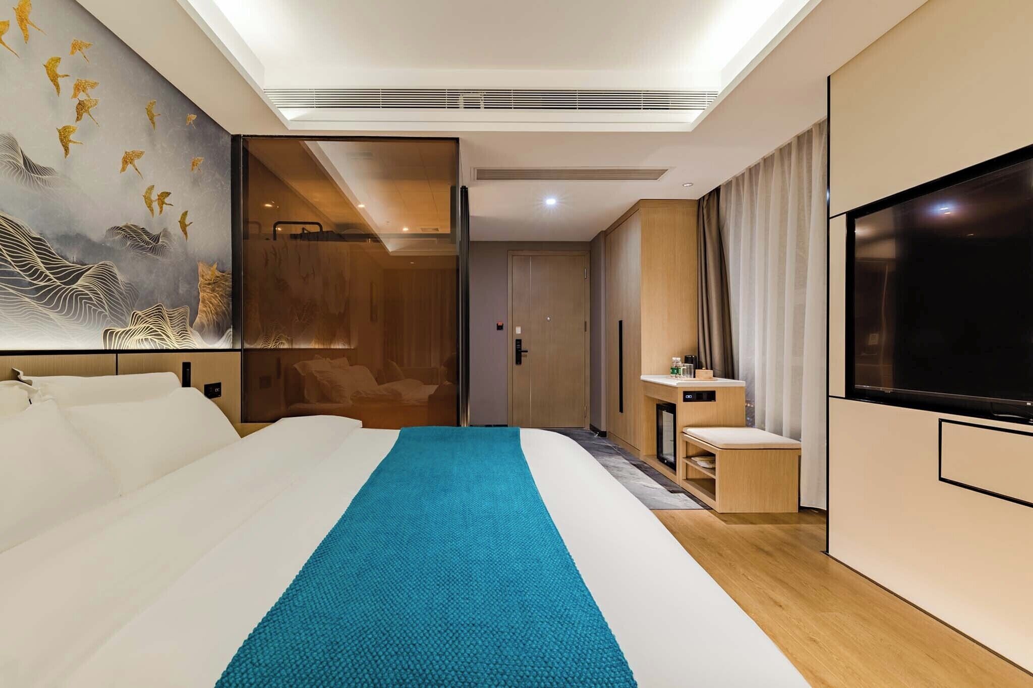 A modern hotel room with a large bed, a TV, a bathroom, and a painting on the wall.