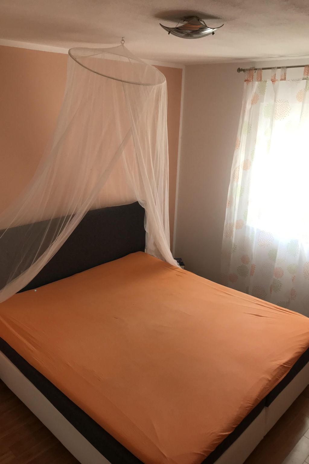 A bed with a canopy, a ceiling fan, and a window with curtains.