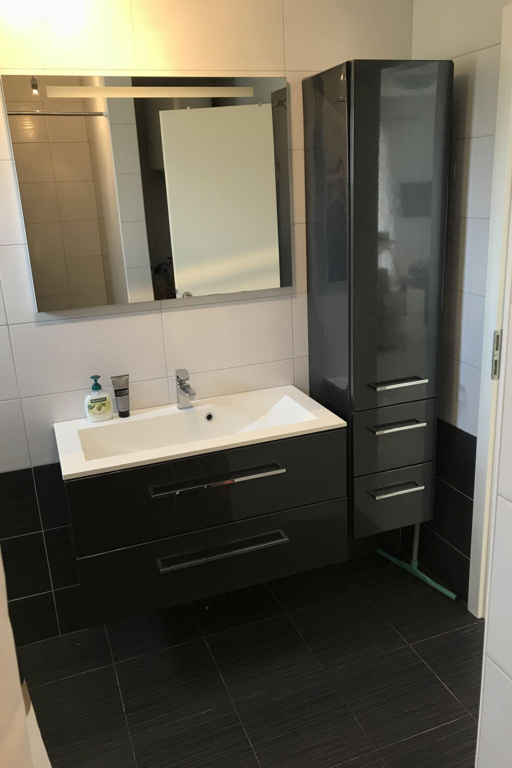Ein modernes Badezimmer mit einem weißen Waschbecken, dunklen Schränken und einem großen Spiegel.