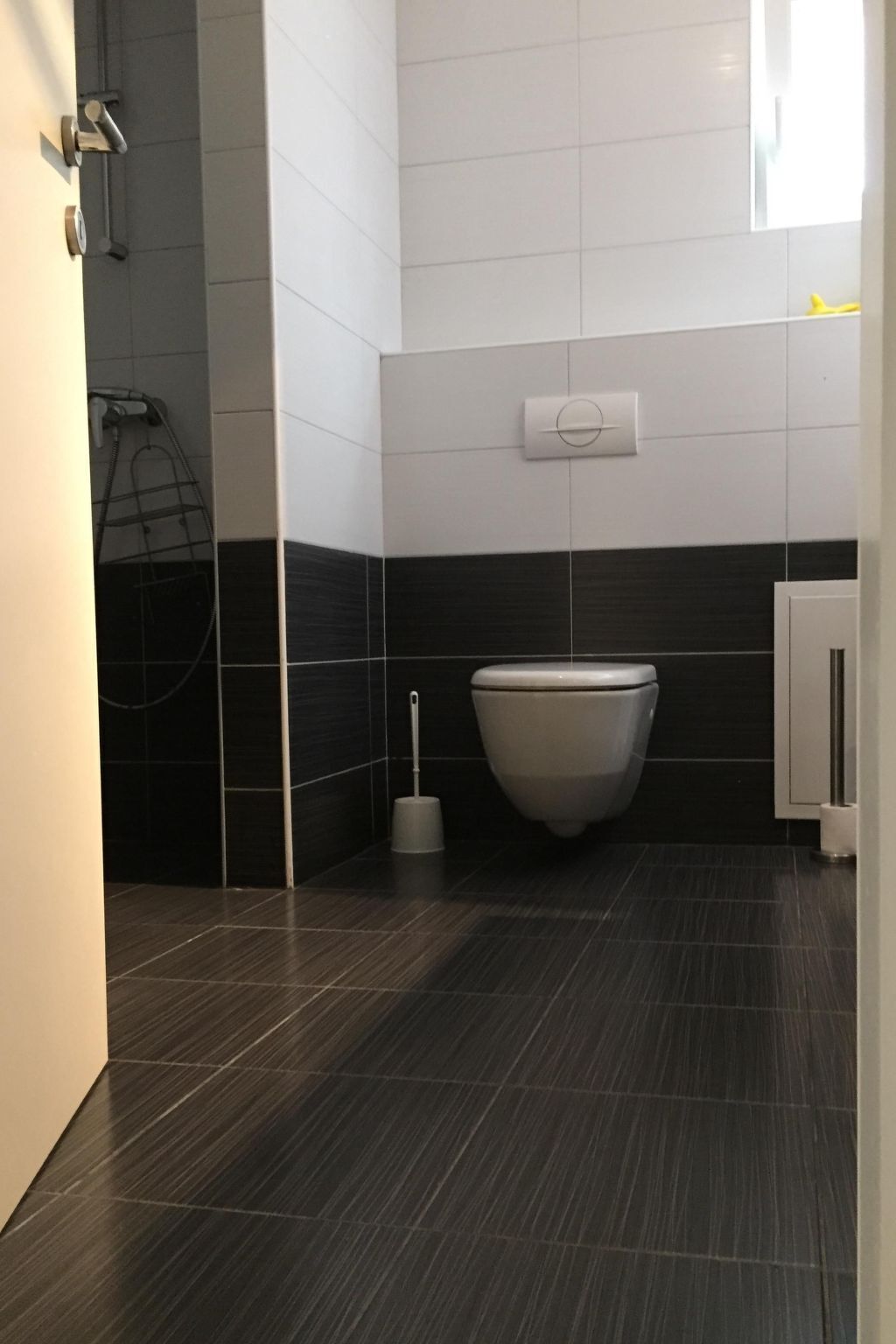 A modern bathroom with a toilet, a hand dryer, and a toilet paper holder.