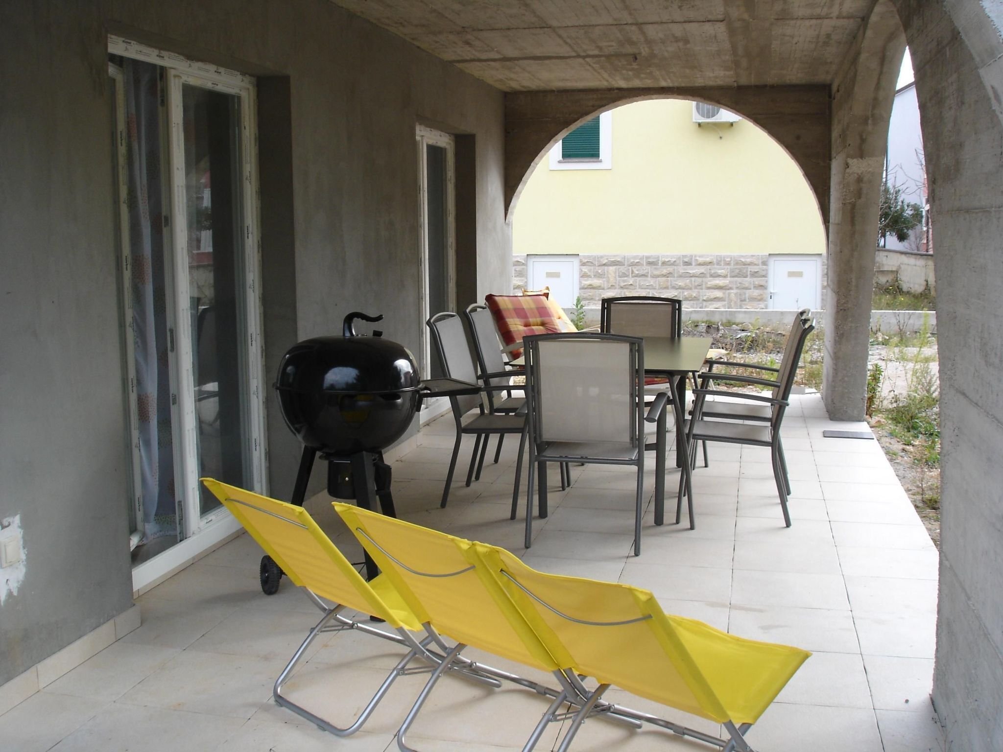 An outdoor patio with a grill, yellow lounge chairs, and a table with chairs.