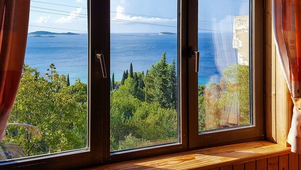 Una habitación con un ventanal grande que da a un paisaje costero, con vegetación y vista al mar.