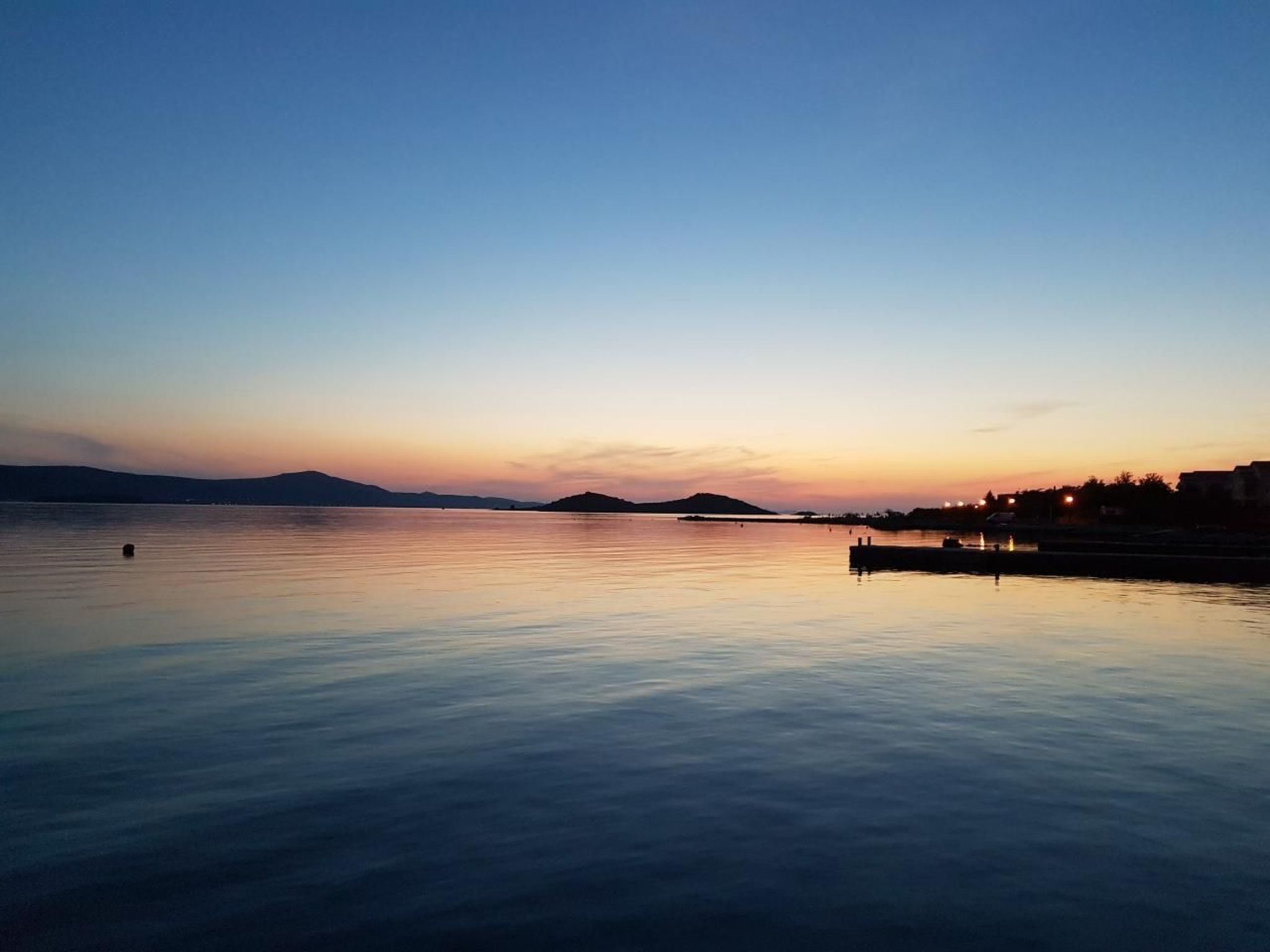 Tyyni järvi auringonlaskun aikaan, etualalla laituri ja taustalla rakennuksia.