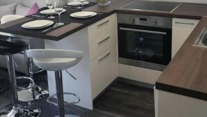 A modern kitchen with white cabinets, a built-in oven, and a dining area with bar stools. - Apartment Sara by Interhome (Zadar)