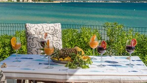 Une table dressée avec des boissons et des fruits sur un balcon donnant sur une vue de la côte.
