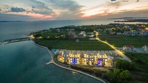 Une vue aérienne d’une zone côtière, avec une rangée de bâtiments modernes, une marina et une route menant aux bâtiments.