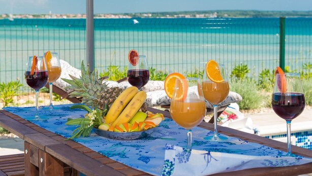Une table placée au bord de la piscine, avec des boissons et des fruits, d’où l’on peut admirer une mer d’un bleu limpide.
