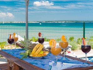 A poolside table with drinks and fruit, overlooking a clear blue sea.