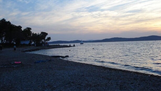 Una platja amb un litoral rocos, un far a la distància i una mar tranquil·la.