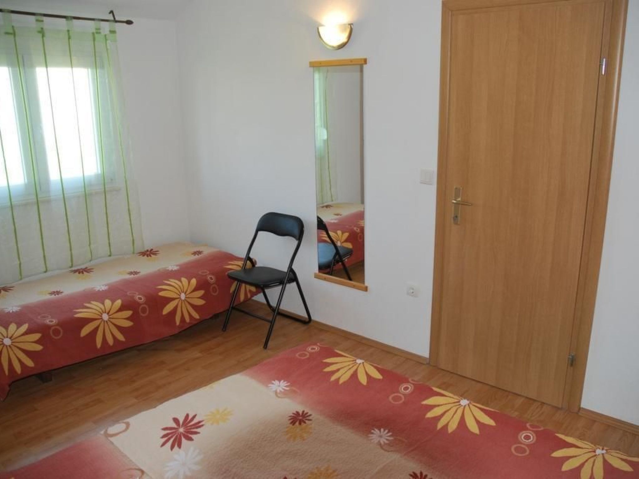 A bedroom with a bed, a chair, a mirror, and a wooden door.