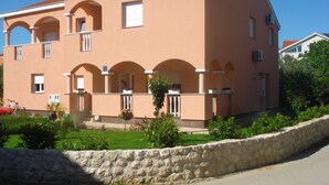 Edifici de dues plantes amb un mur de pedra al davant, un balcó amb plantes en testos i un cel blau clar.