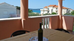 Un balcó amb taula preparada per a dues persones, amb vista al mar, edificis i cel blau.