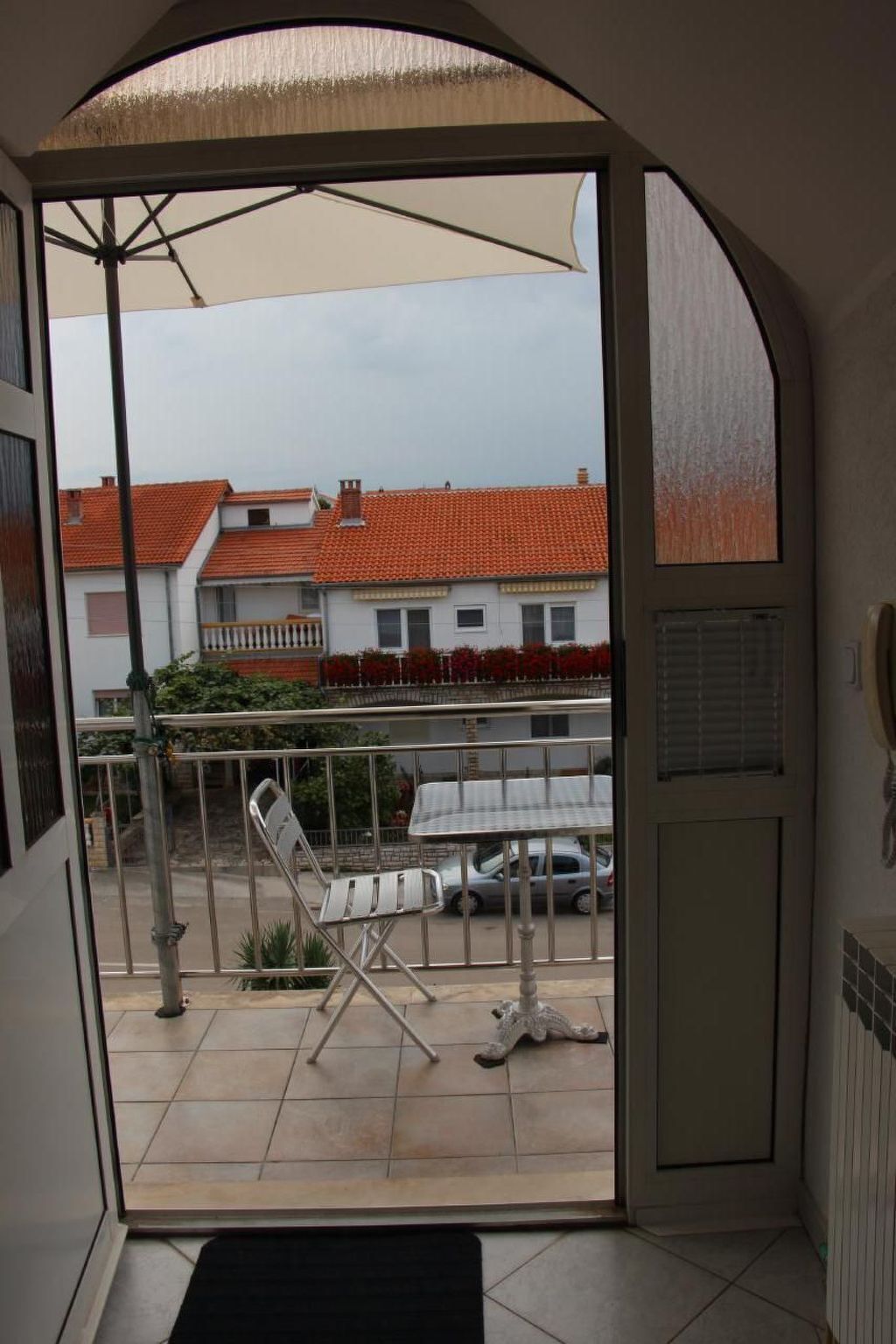 A balcony with a view of a residential area, a metal railing, and a white chair.
