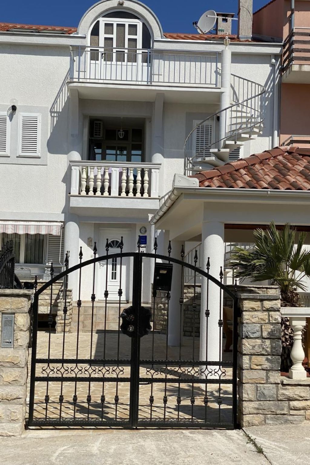 Une maison à deux étages, avec une façade blanche, un balcon et un portail d’entrée en pierre.
