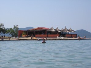 Un hotel sul lungomare con area piscina, un bar e diverse strutture con tetto di paglia.