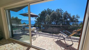 Un balcon avec une porte-fenêtre, une table, des chaises et un transat.