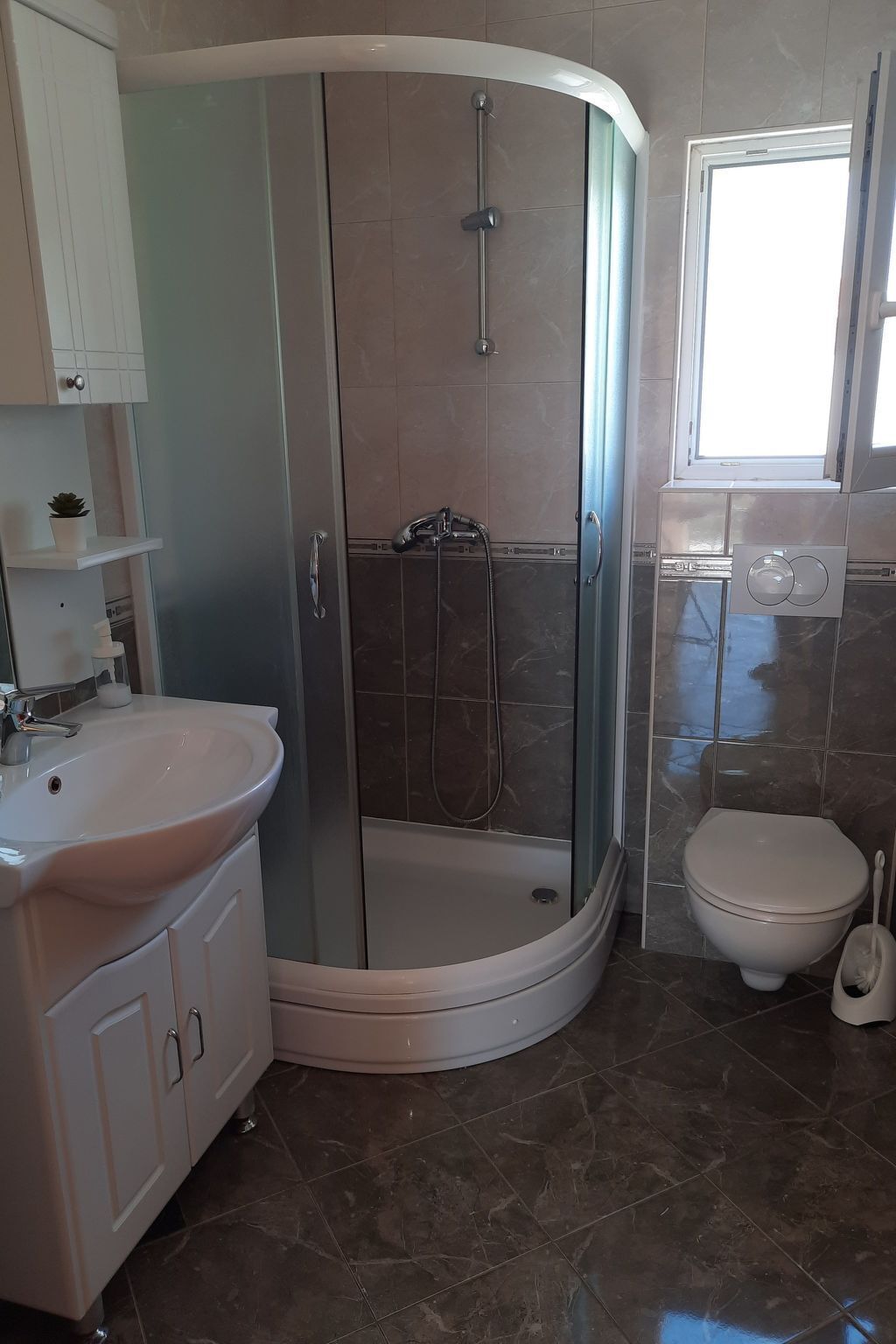 A bathroom with a glass-enclosed shower, a sink, a toilet, and a window.