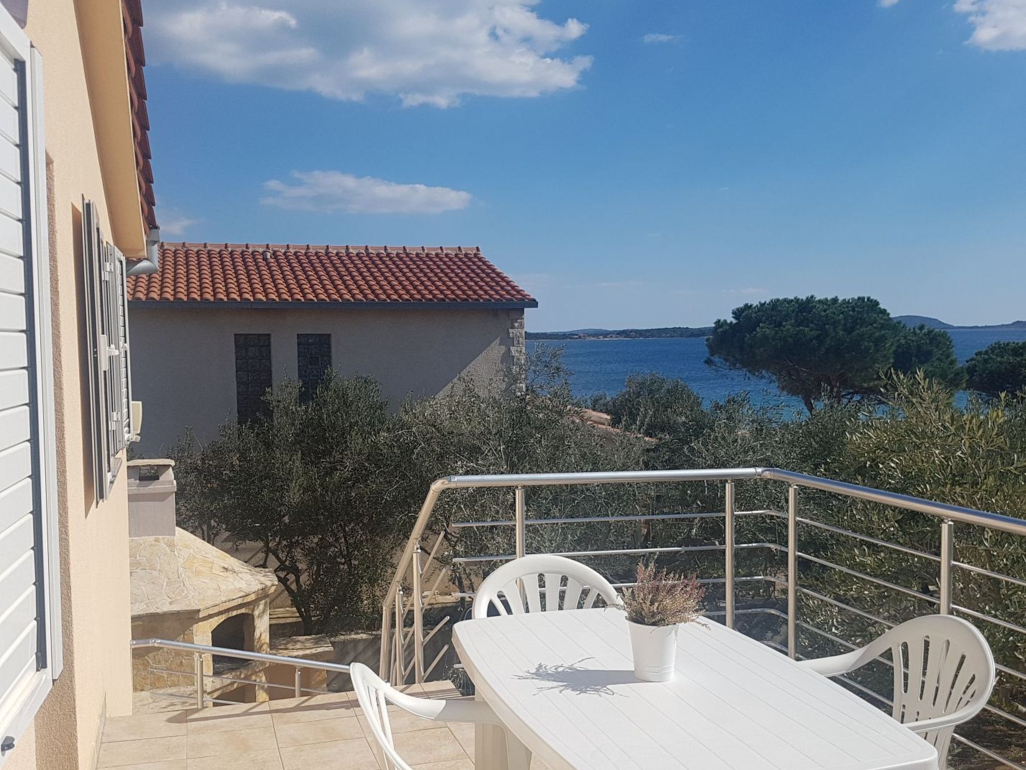 A balcony with a white table and chairs, overlooking a body of water and a distant island.