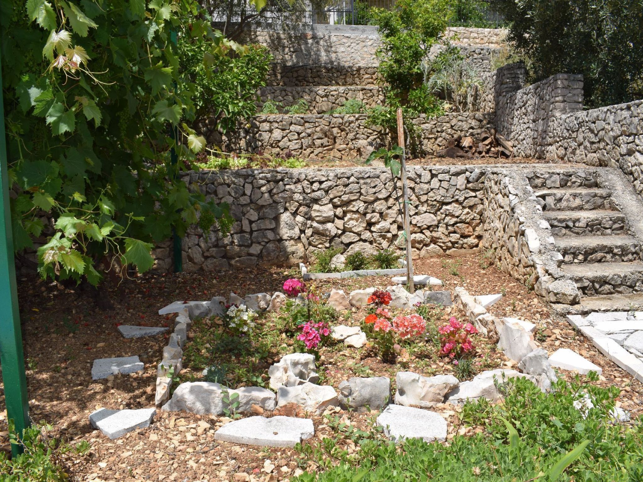 Ein Garten mit Steinmauern, einer Pergola und blühenden Pflanzen.