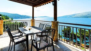 Un espacio de comedor al aire libre cubierto, con mesa y sillas, con vistas a una masa de agua y colinas.