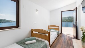 Un dormitorio con dos camas de madera, un ventanal con vistas al mar y un balcón también con vistas al mar.