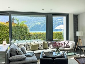 En moderne stue med sofa, sofabord og udsigt til et bjerrelandskab gennem store vinduer.
