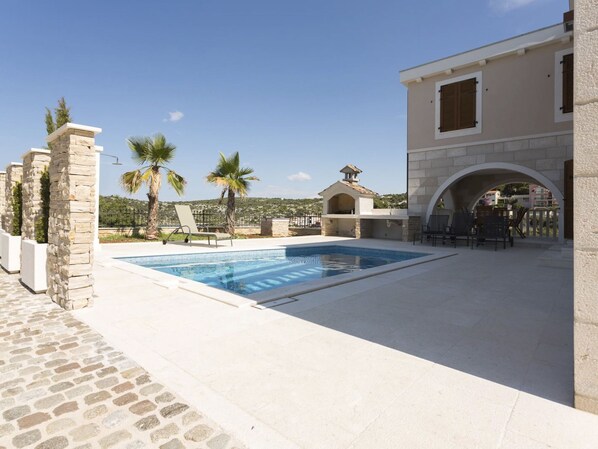 Une piscine avec des chaises longues, un espace barbecue et des piliers en pierre.